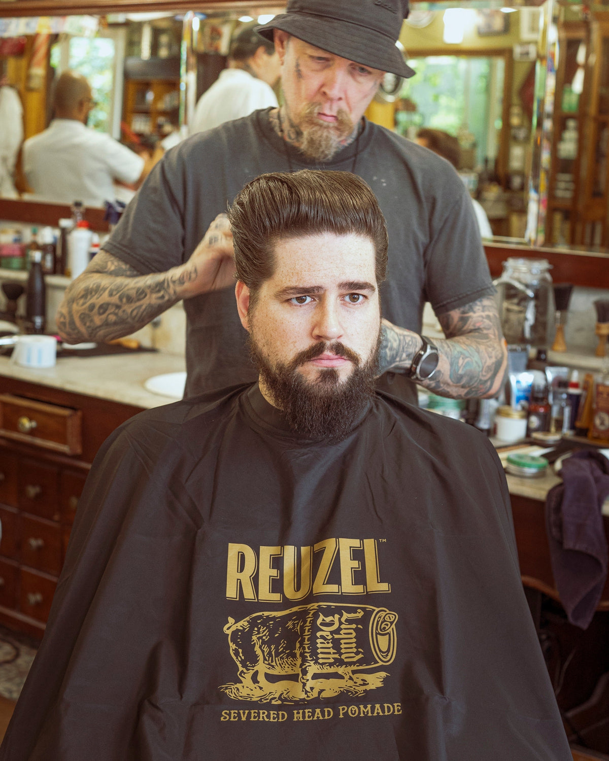 Severed head Reuzel barber cape from REUZEL, featuring bold graphic design, used as a stylish hairdressing accessory or merchandise.