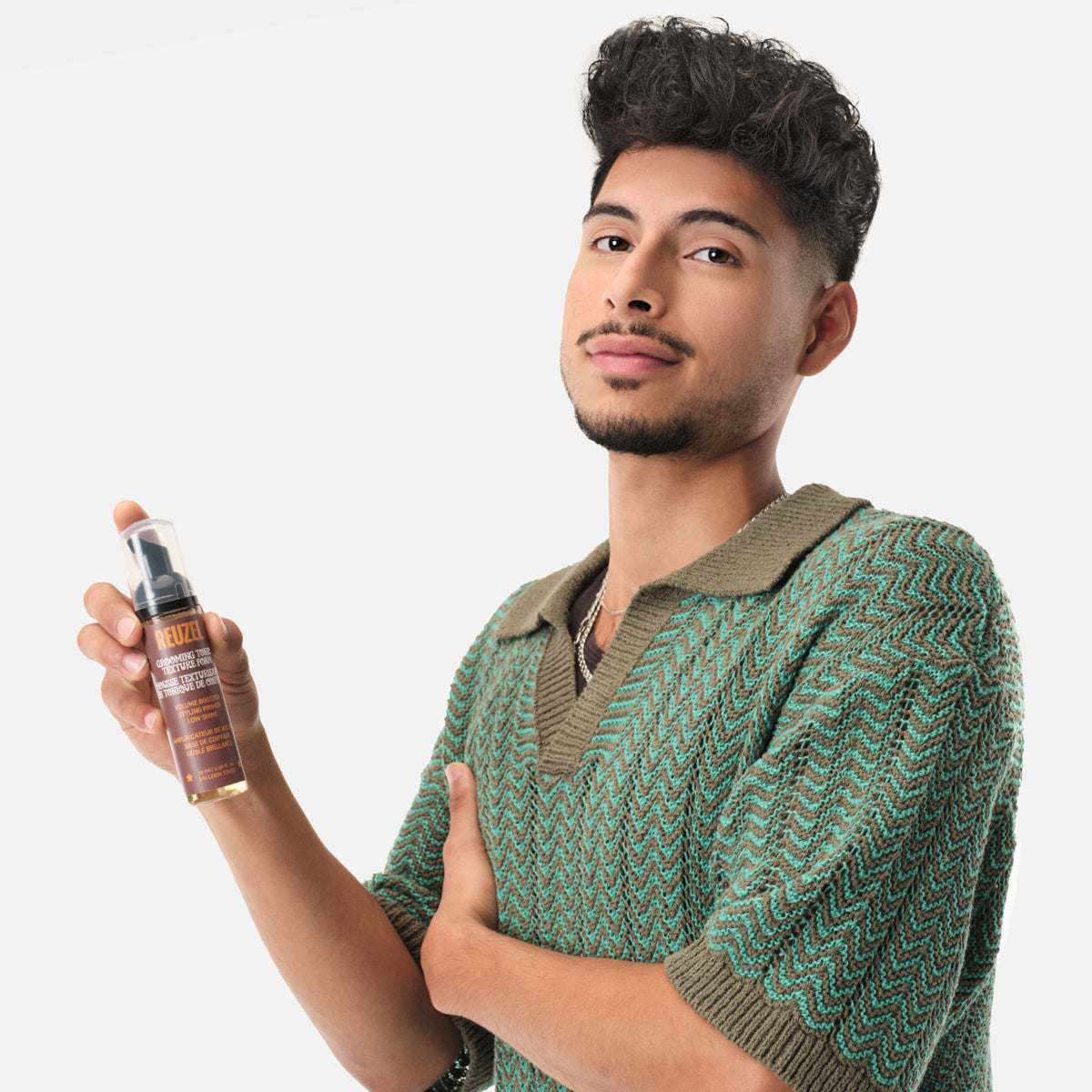 Man holding a bottle of Reuzel Grooming Tonic Texture Foam hair product against a plain background