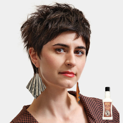 Woman with short hair and large earrings, with a bottle of Reuzel Daily Conditioner  in the corner.
