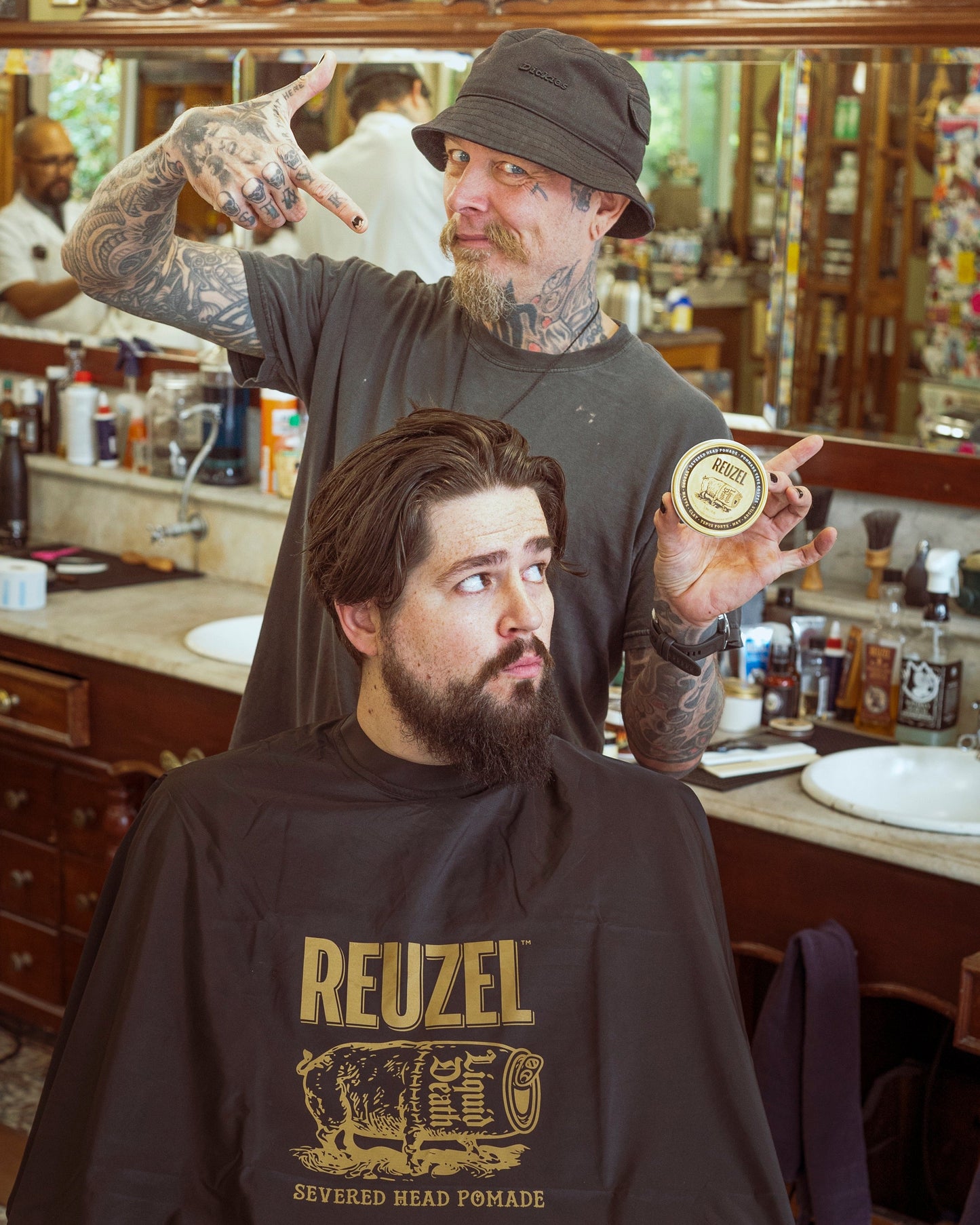 Severed head Reuzel UK barber cape with graphic design, used as stylish merch for barber and grooming enthusiasts.