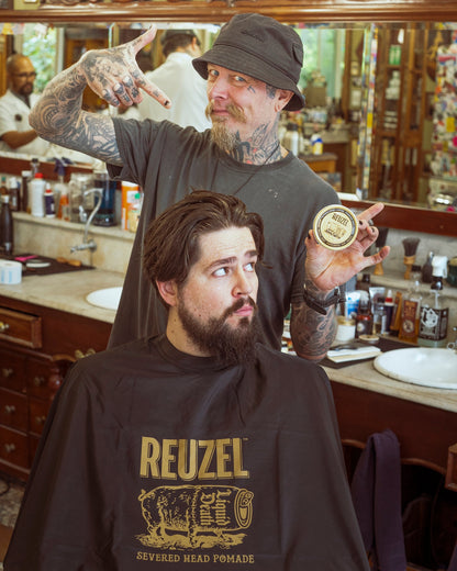 Severed head Reuzel barber cape with graphic design, used as stylish merch for barber and grooming enthusiasts.