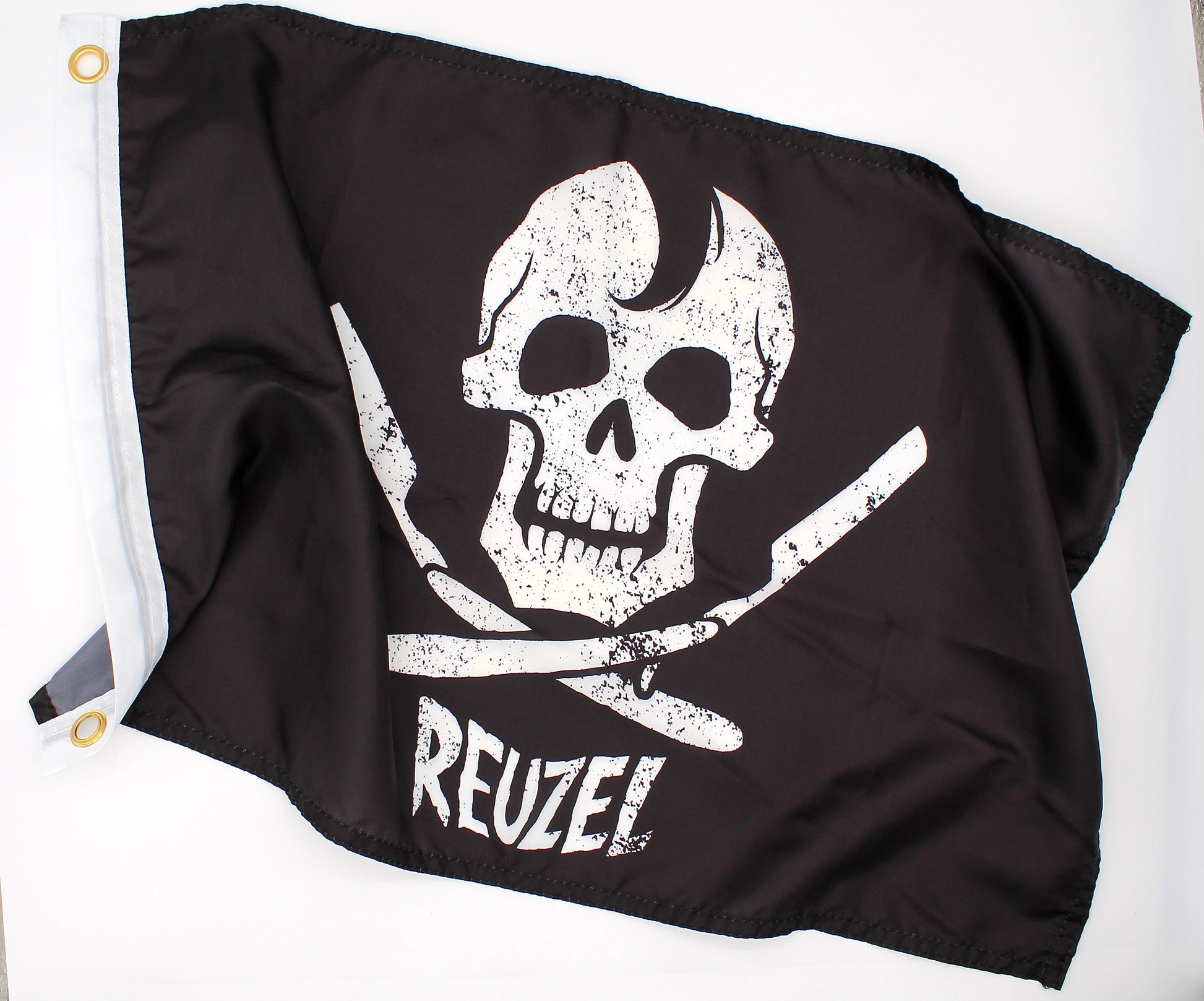 Black pirate flag with a white skull and open razors design and 'REUZEL' branding on a white background.