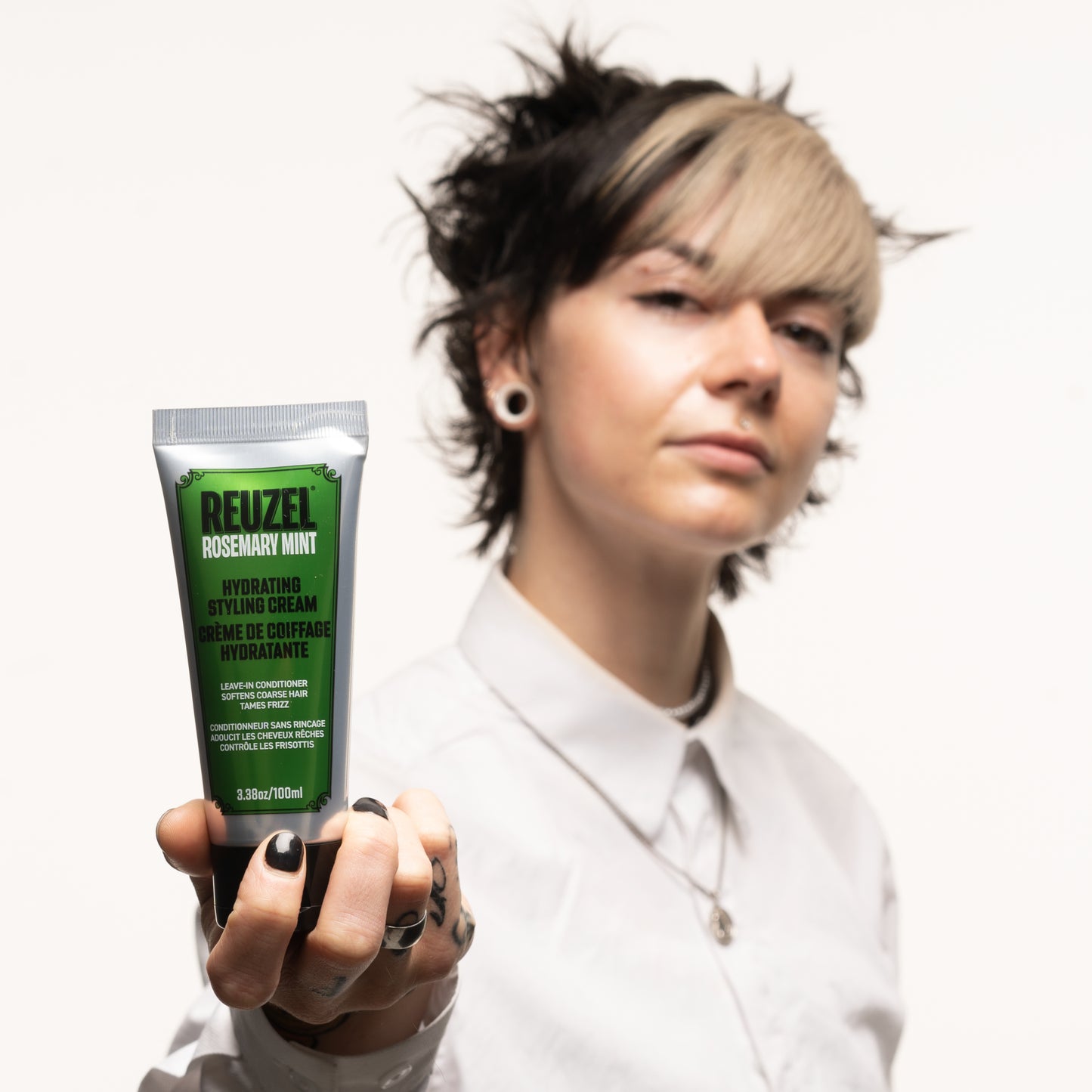 Person holding a tube of Reuzel Hydrating Styling Cream against a neutral background