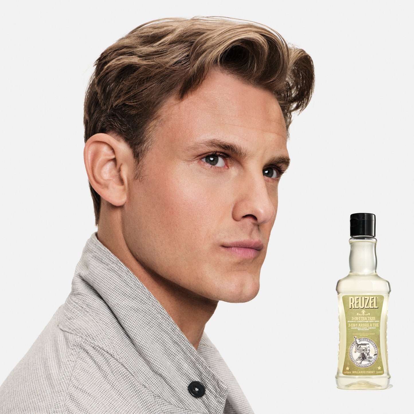 Man with styled hair next to a bottle of REUZEL 3 in 1 Shampoo product on a white background