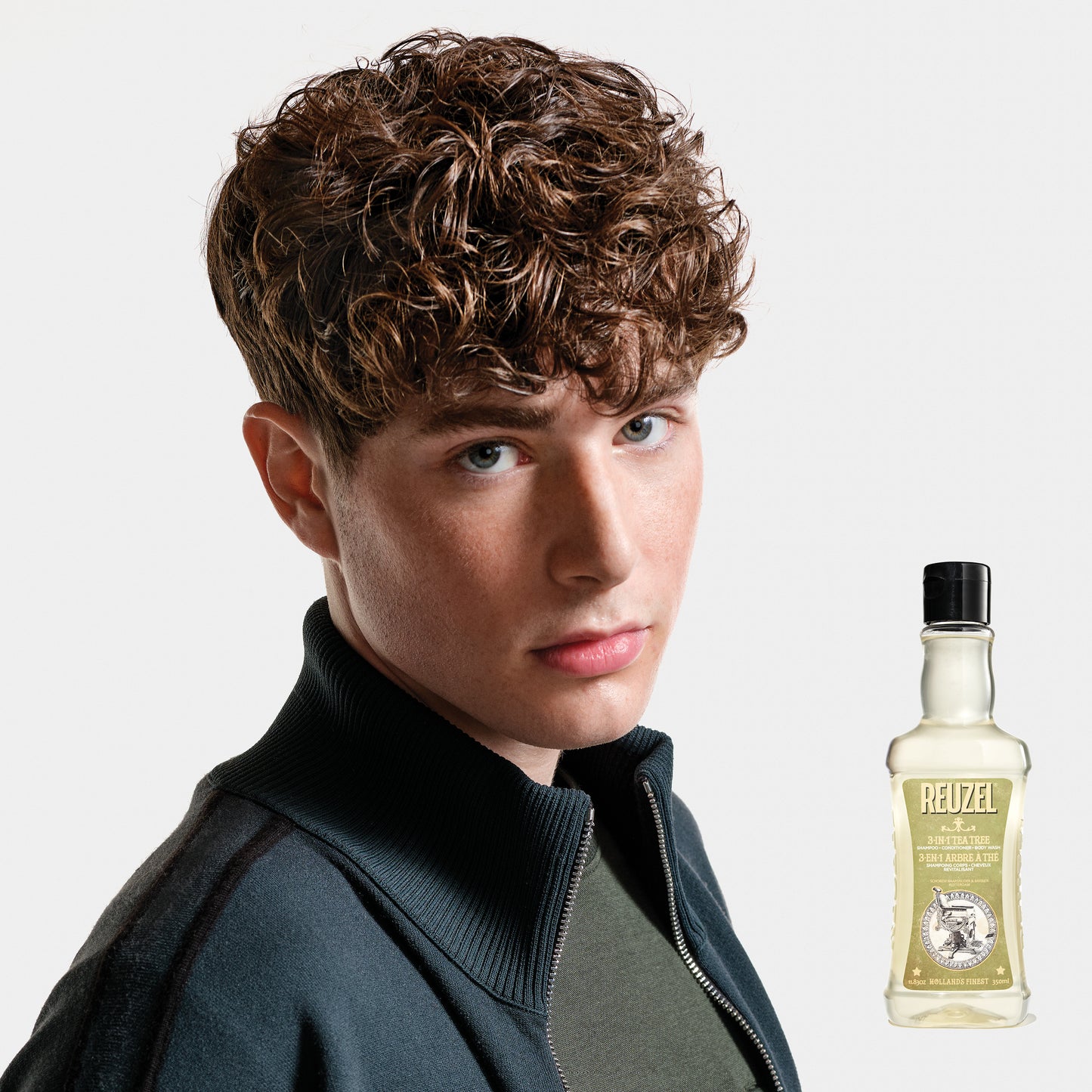 Person with styled hair next to a bottle of REUZEL 3 in 1 Shampoo on a white background