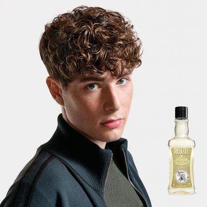 Person with styled hair next to a bottle of REUZEL 3 in 1 Shampoo on a white background