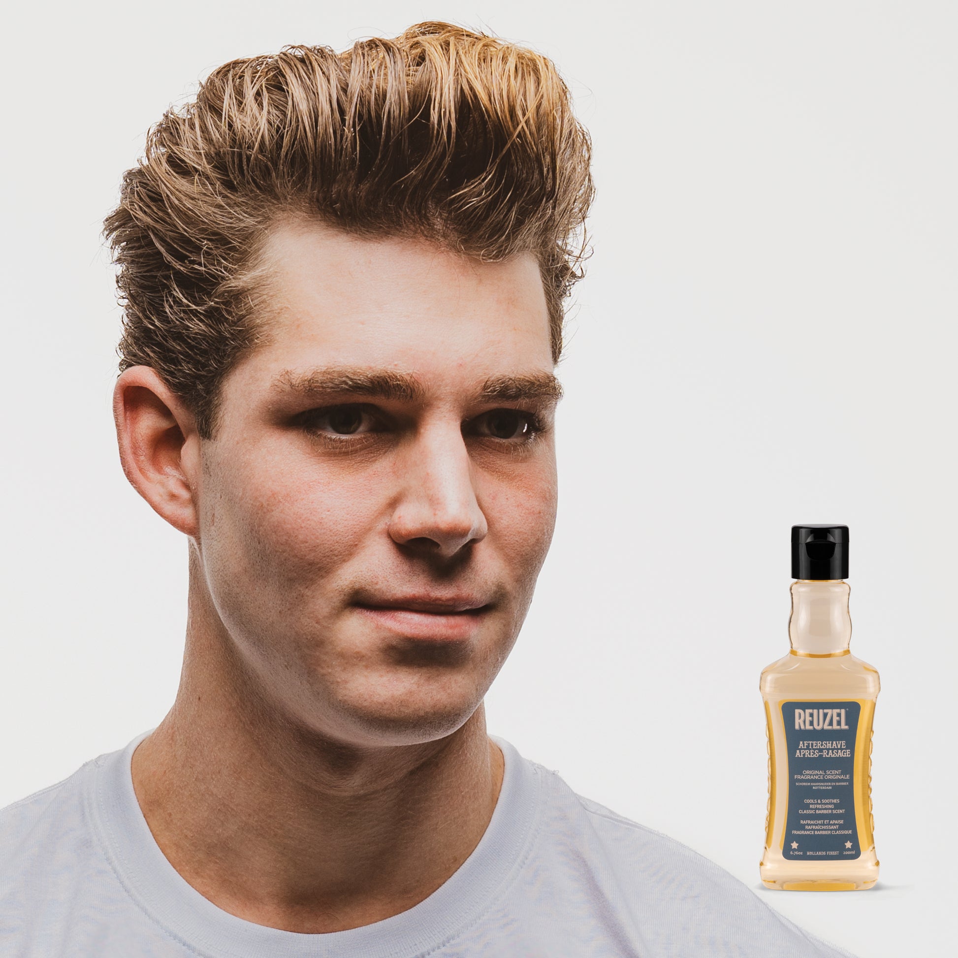 Man with styled hair next to a bottle of Reuzel Aftershave on a white background