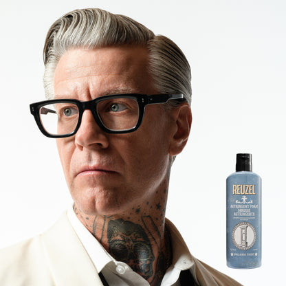 Man with styled hair and glasses next to a bottle of Reuzel Astringent Foam on a white background