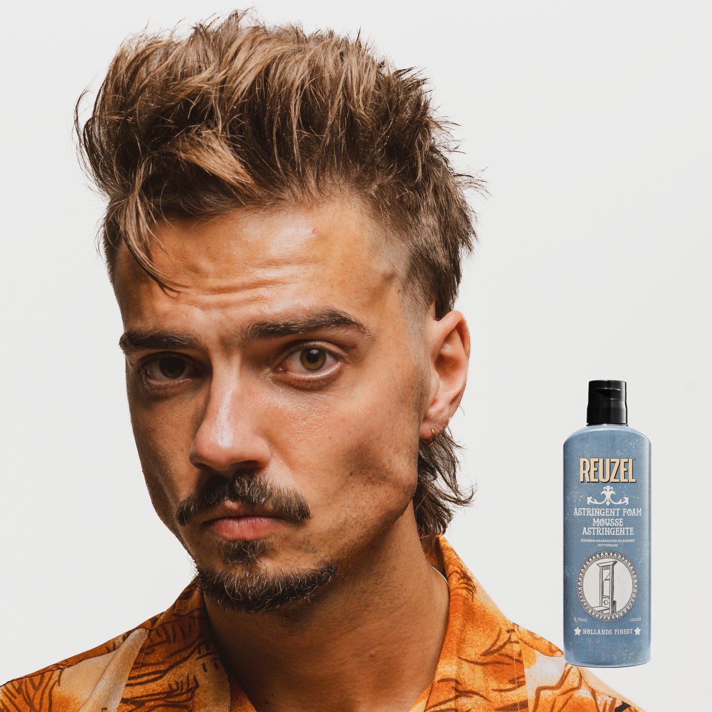 Man with styled hair next to a bottle of Reuzel Astringent Foam on a white background