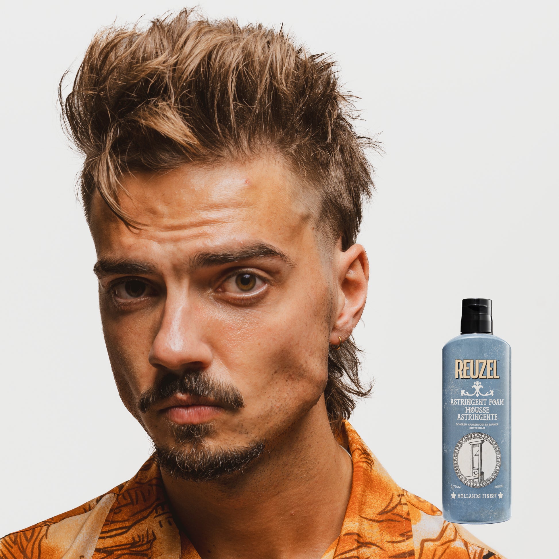 Man with styled hair next to a bottle of Reuzel Astringent Foam on a white background
