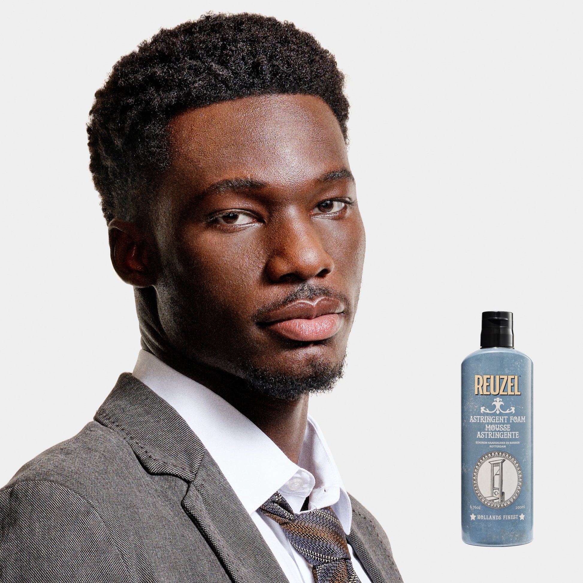 Man in a suit with a bottle of Reuzel Astringent Foam on a white background
