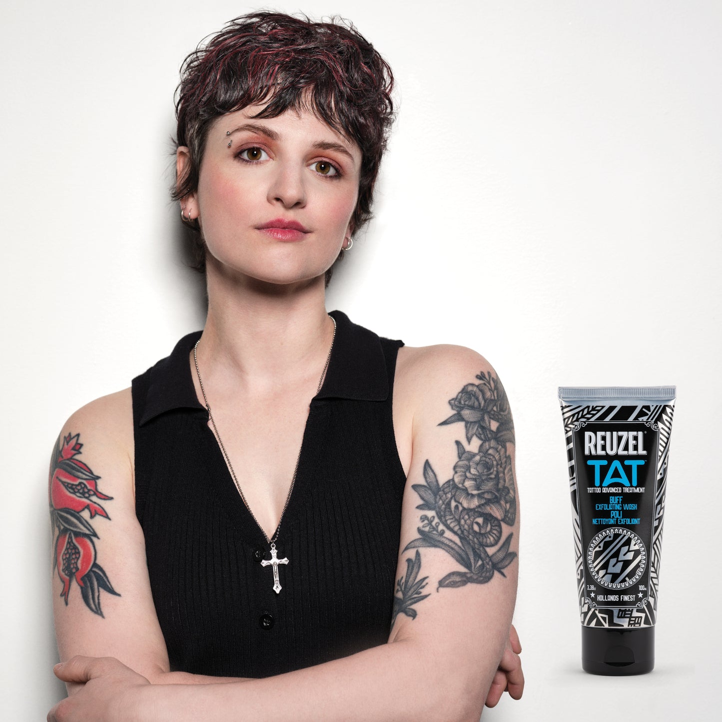 Woman with tattoos wearing a black sleeveless top, next to a Reuzel tattoo aftercare product BUFF.