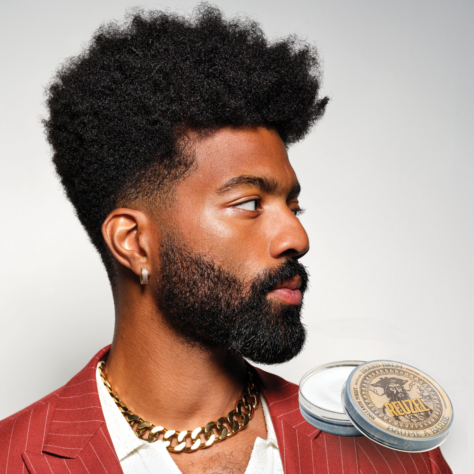 Man with a beard and red jacket with a Reuzel Beard Balm on a light grey background