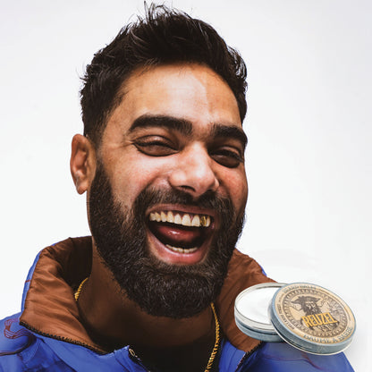 Man with a beard and a blue jacket next to two containers of Reuzel Beard Balm