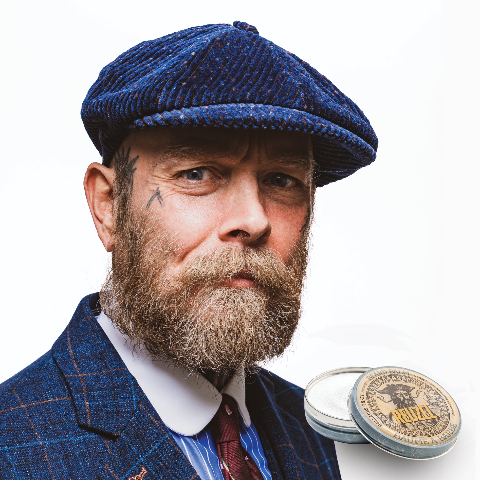 Man wearing a blue checkered cap and suit with a beard, next to a Reuzel Beard Balm on a white background