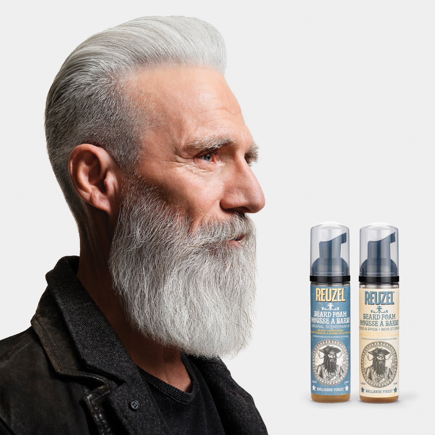 Man with a gray beard and two bottles of Reuzel Beard Foam on a light gray background