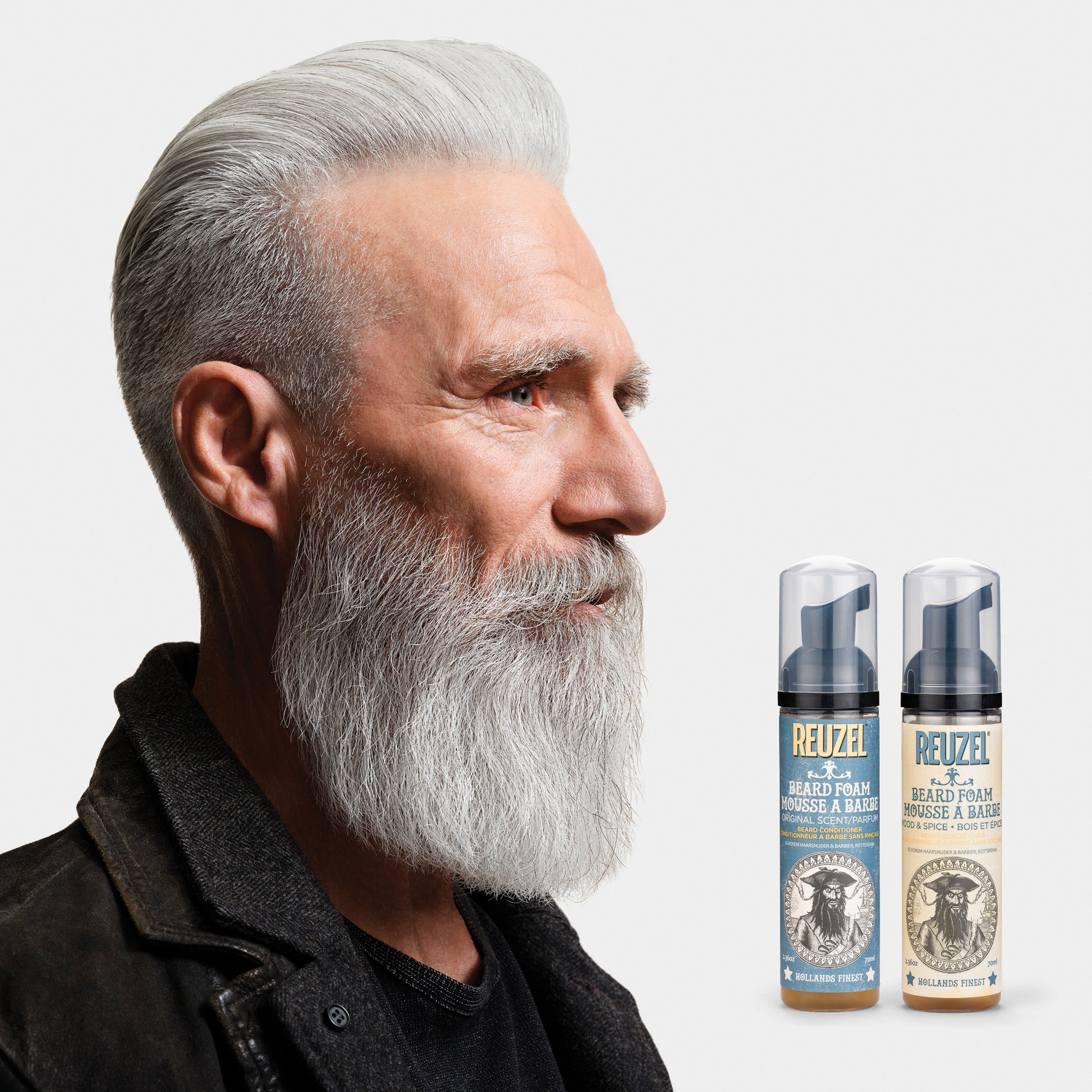 Man with a gray beard and two bottles of Reuzel Beard Foam on a light gray background