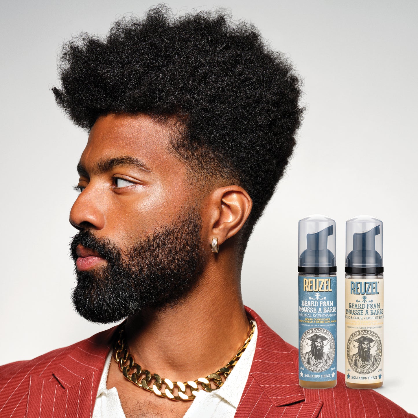 Man with styled hair and beard wearing a red jacket with Reuzel Beard Foam displayed.