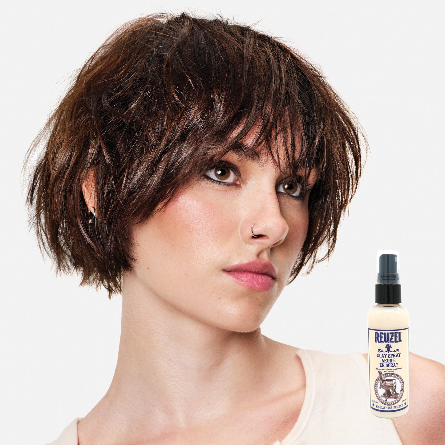 Woman with styled hair next to a bottle of Reuzel Clay Spray on a white background