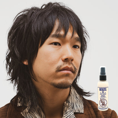 Man with styled hair next to a bottle of Reuzel Clay Spray on a white background