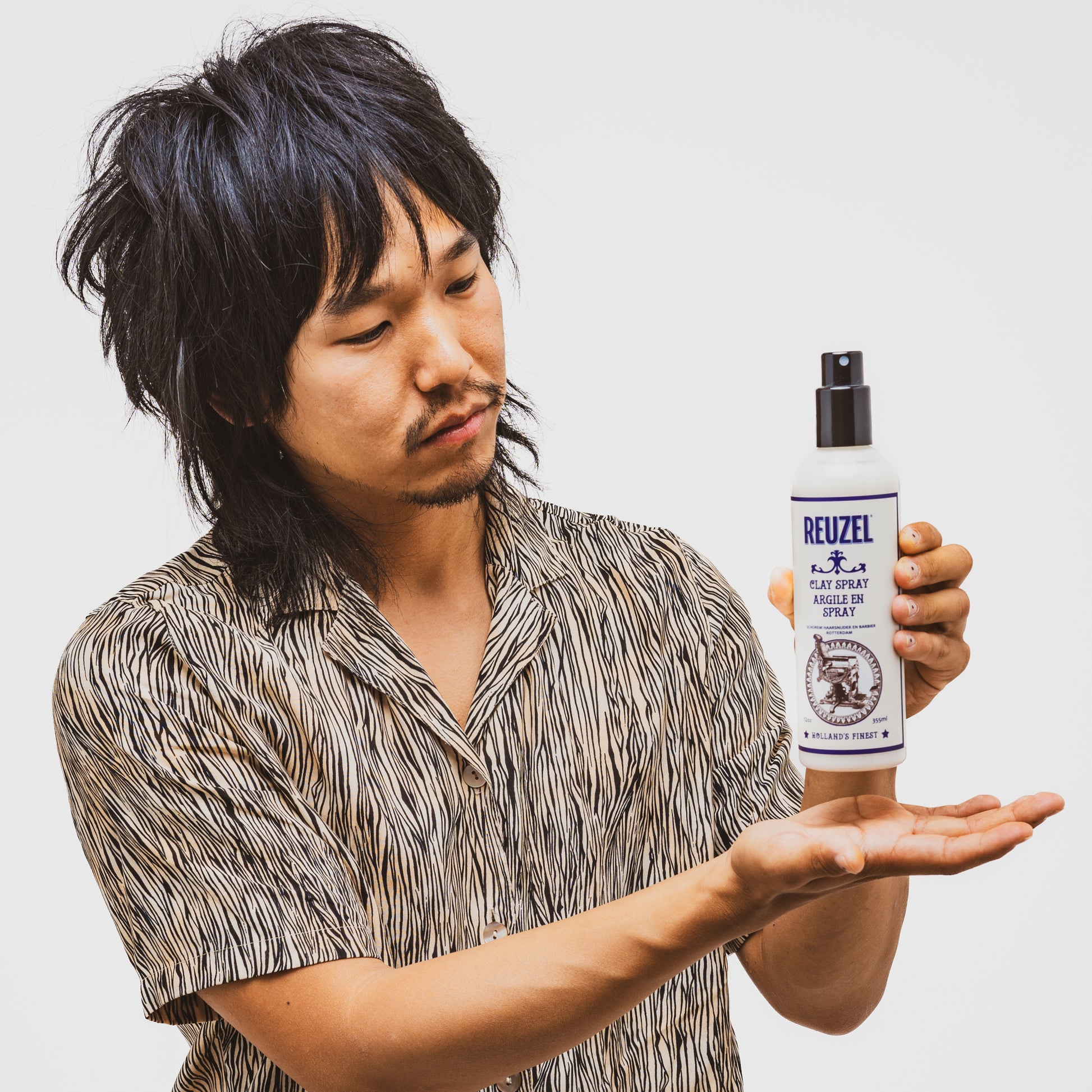 Man holding a bottle of Reuzel Clay Spray against a plain background