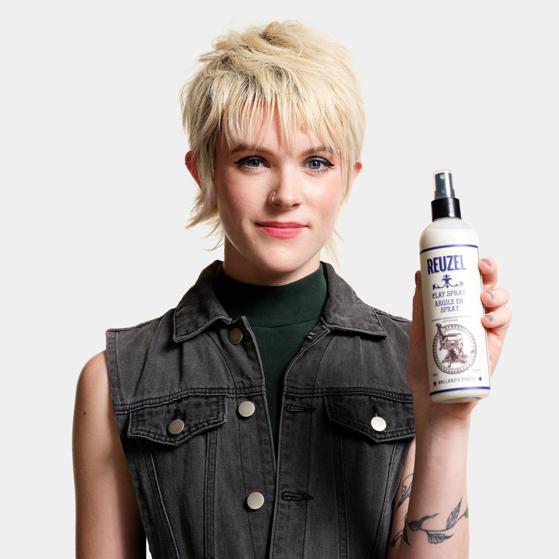 Person holding a bottle of Reuzel Clay Spray against a plain background