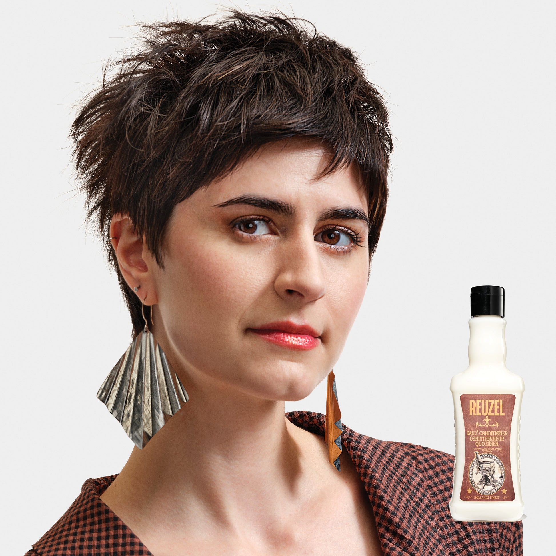 Woman with styled hair next to a bottle of Reuzel Daily Conditioner on a white background