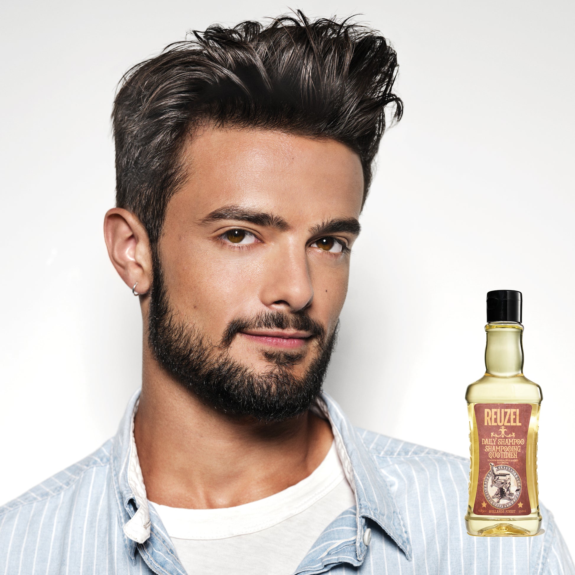 Man with styled hair and a bottle of Reuzel Daily Shampoo on a white background