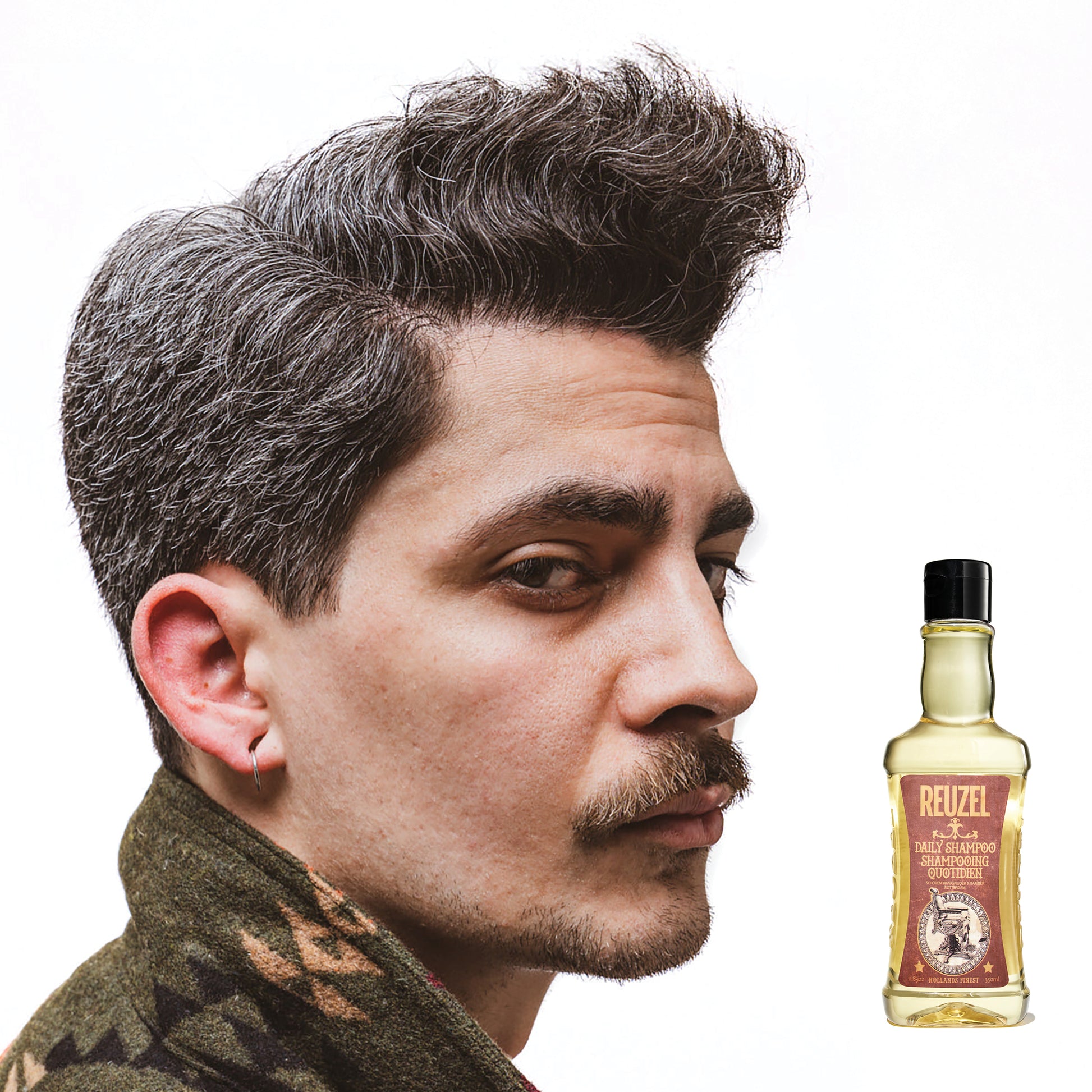 Side profile of a man with styled hair and a patterned shirt with a bottle of Reuzel Daily Shampoo on a white background