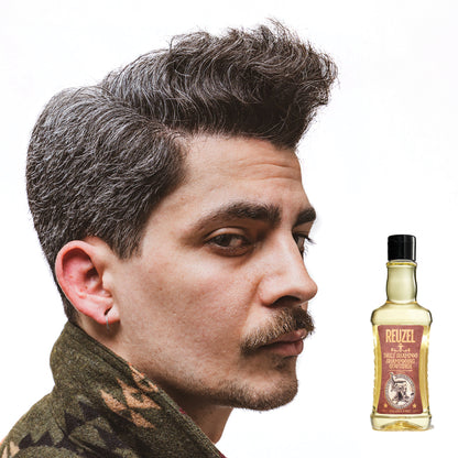 Side profile of a man with styled hair and a patterned shirt with a bottle of Reuzel Daily Shampoo on a white background
