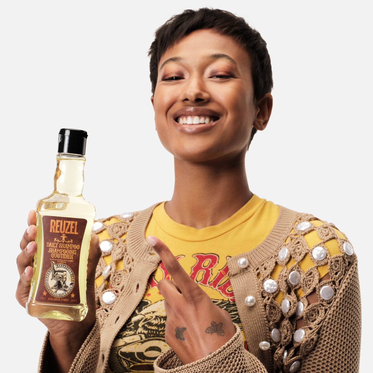 Person holding a bottle of Reuzel Daily Shampoo with a neutral background