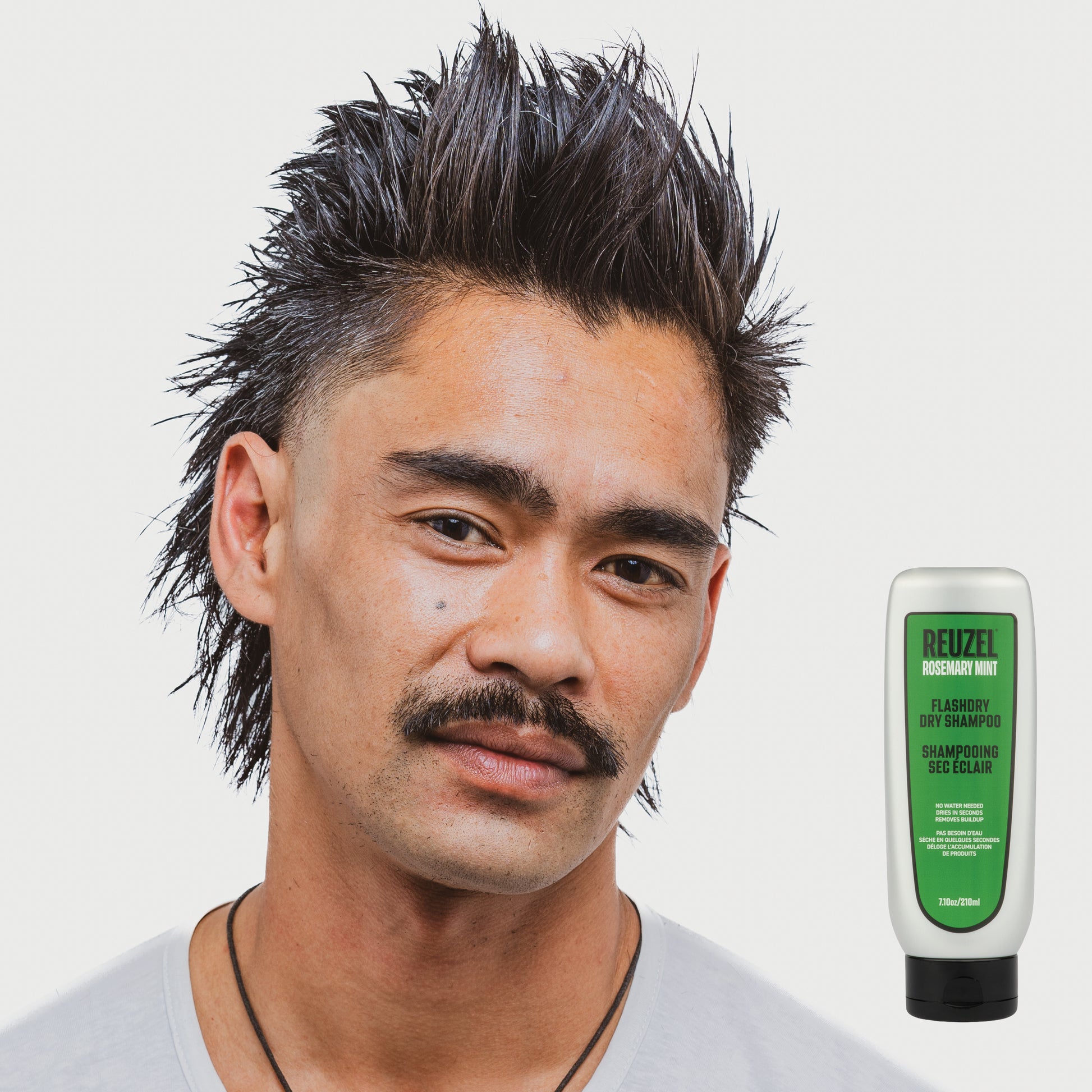 Man with styled hair next to a bottle of REUZEL FLASHDRY shampoo product on a white background