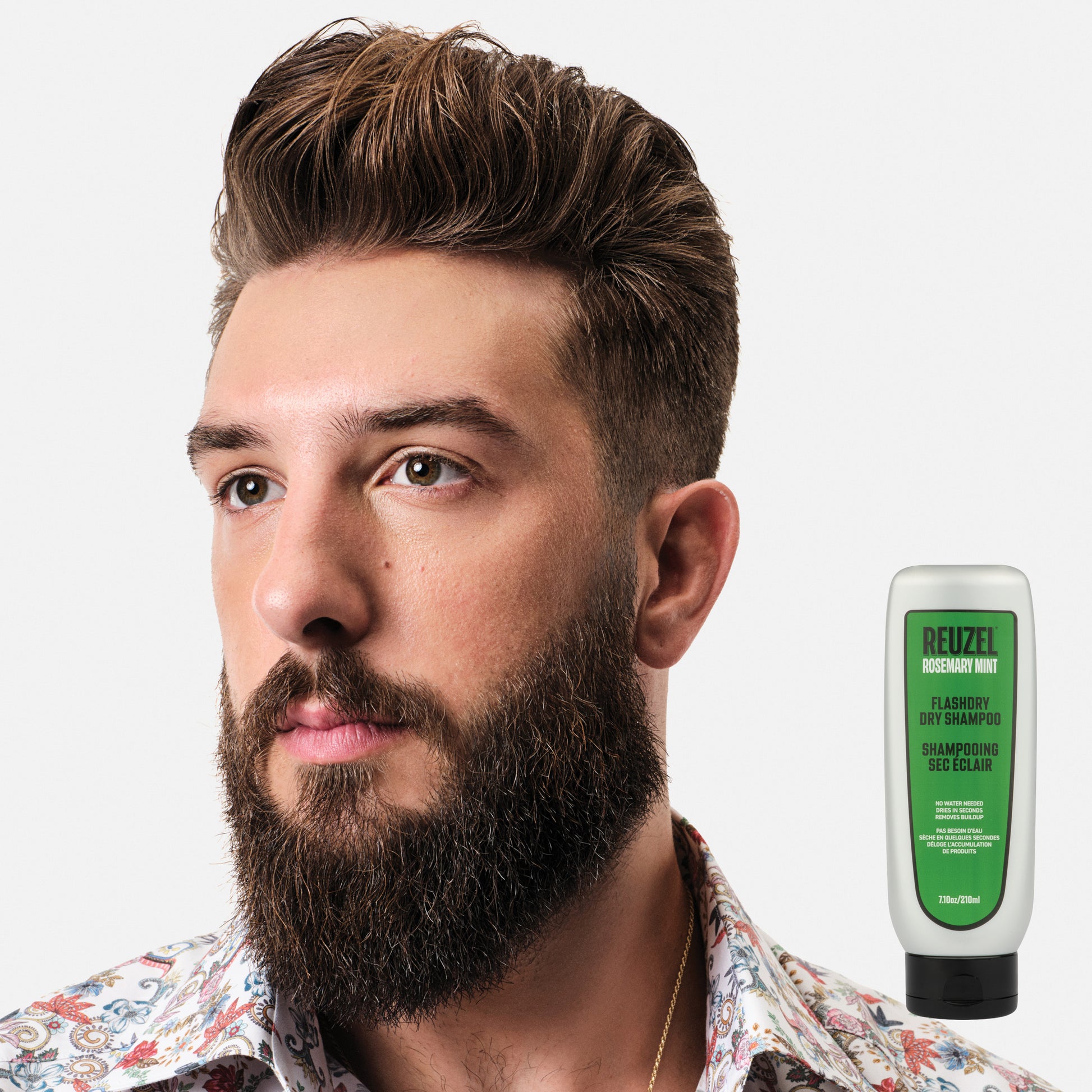 Man with a beard and hairstyle, with a bottle of Reuzel FLASHDRY on a white background