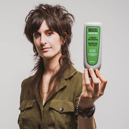 Woman holding a bottle of Reuzel Flashdry Dry Shampoo against a plain background