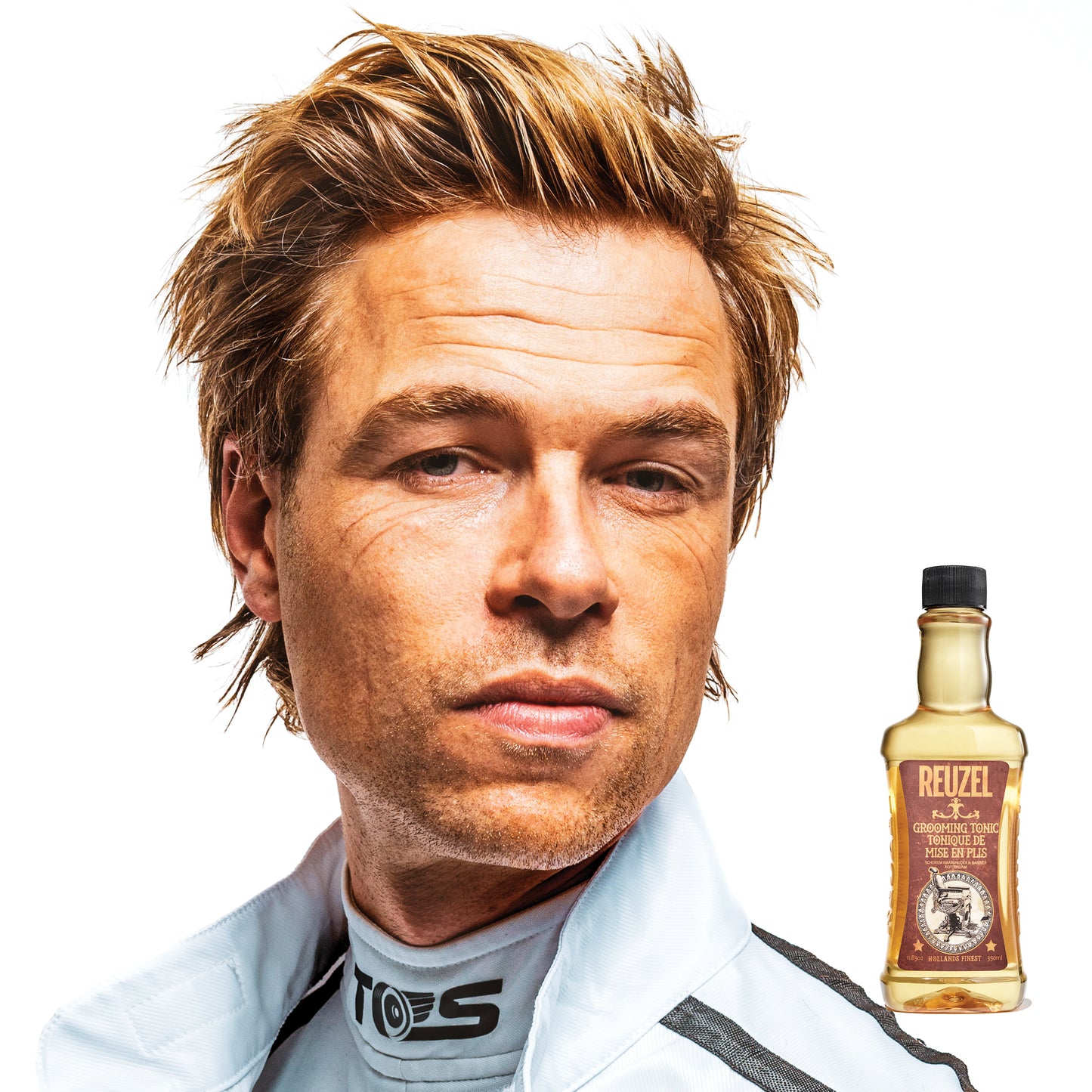Man with blonde hair and a bottle of Reuzel Grooming Tonic on a white background