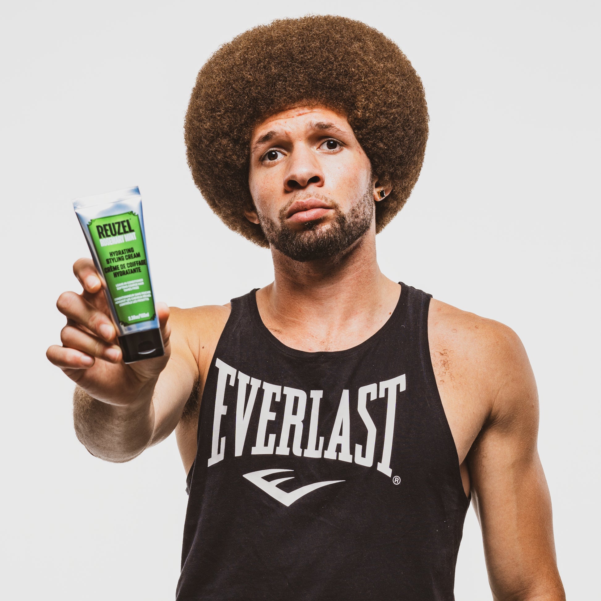 Man holding a product labeled 'Reuzel' Styling Cream against a plain background