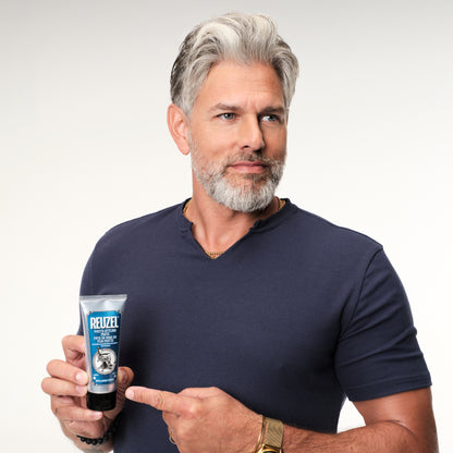 Man holding a tube of Reuzel Matte Styling Paste against a plain background