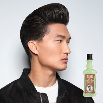 Man with styled hair next to a bottle of REUZEL Scrub Shampoo on a white background