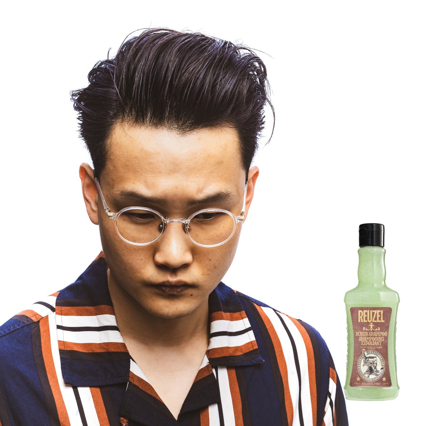 Man with styled hair and glasses next to a bottle of Reuzel Scrub Shampoo on a white background