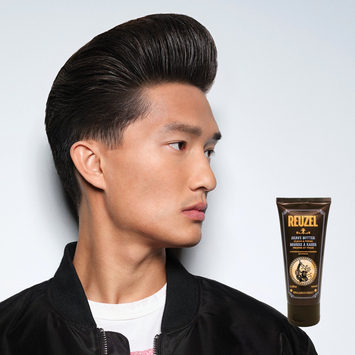 Man with styled hair next to a tube of Reuzel Shave Butter on a light gray background