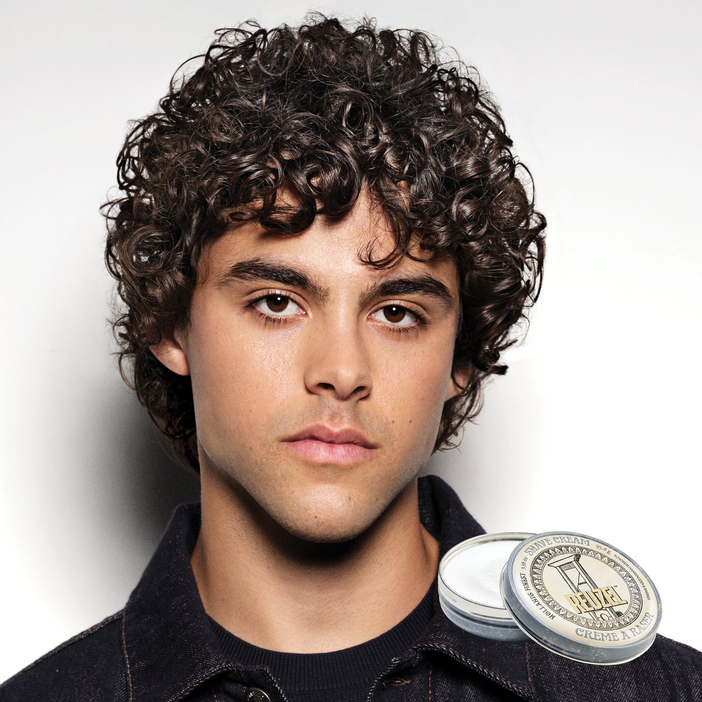Man with styled hair next to a jar of Reuzel Shave Cream on a white background