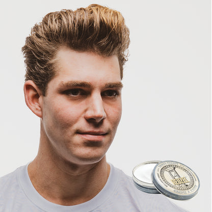 Man with styled hair next to a container of Reuzel Shave Cream on a white background