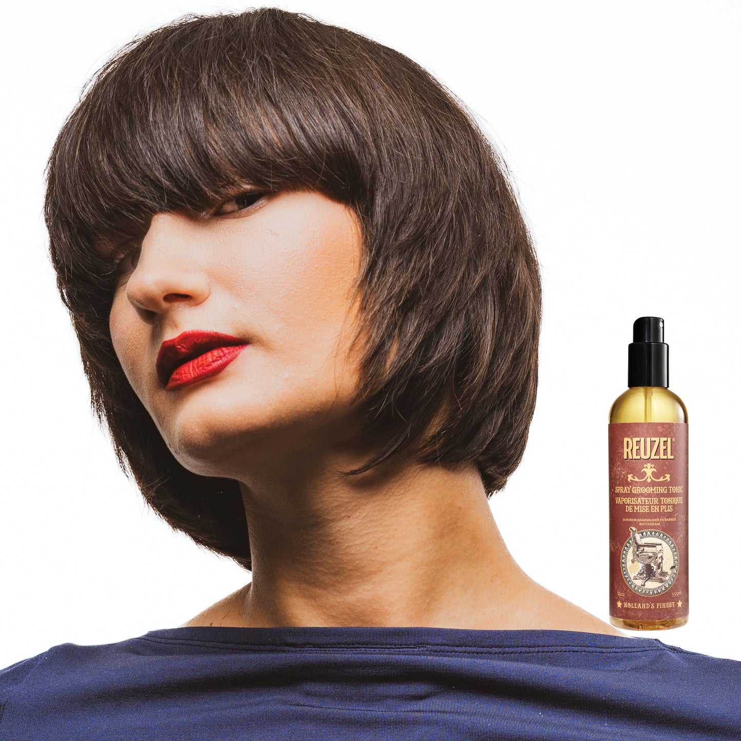Woman with short brown hair and red lipstick next to a bottle of Reuzel Spray Grooming Tonic on a white background