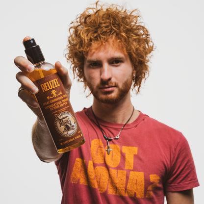 Man holding a bottle of Reuzel Spray Grooming Tonic against a plain background