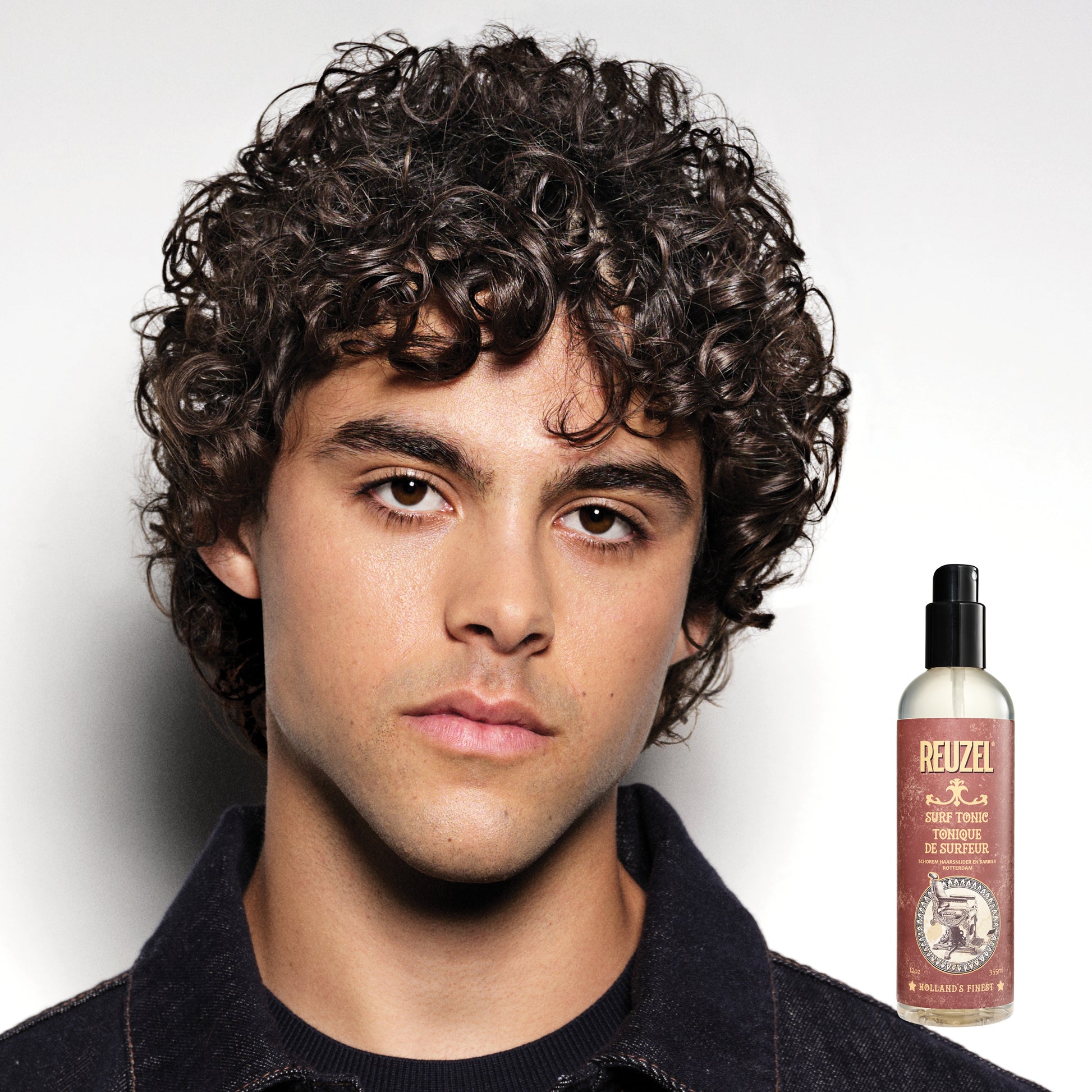 Man with styled hair next to a bottle of Reuzel Surf Tonic on a white background