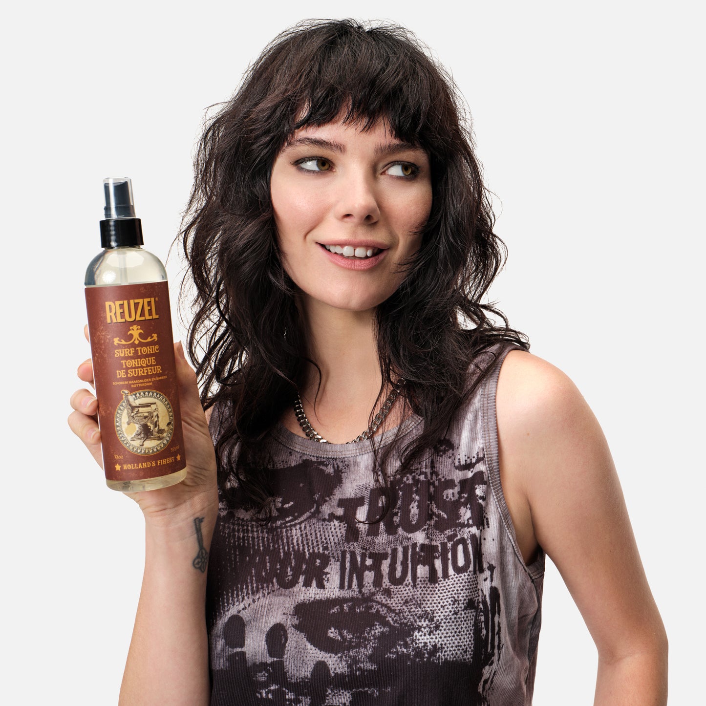 Woman holding a bottle of Reuzel Surf Tonic against a plain background