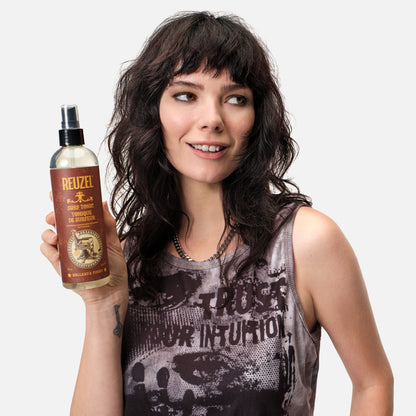 Woman holding a bottle of Reuzel Surf Tonic against a plain background