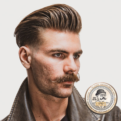 Man with styled hair and mustache wearing a leather jacket, with a tin of Reuzel Mustache Wax