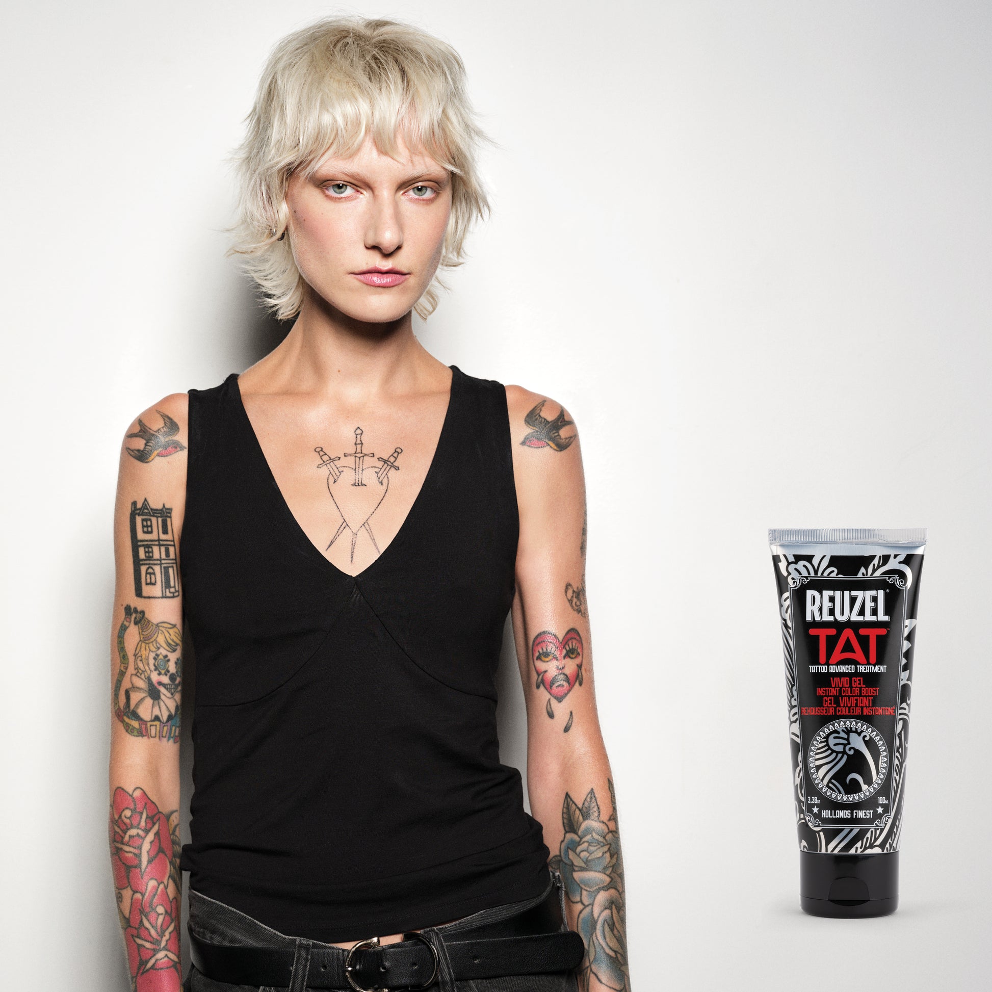 Person with tattoos wearing a black tank top, next to a Reuzel TAT VIVID product on a white background