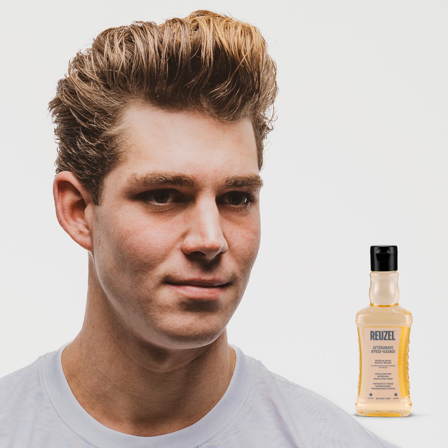 Man with styled hair next to a bottle of Reuzel Aftershave on a white background